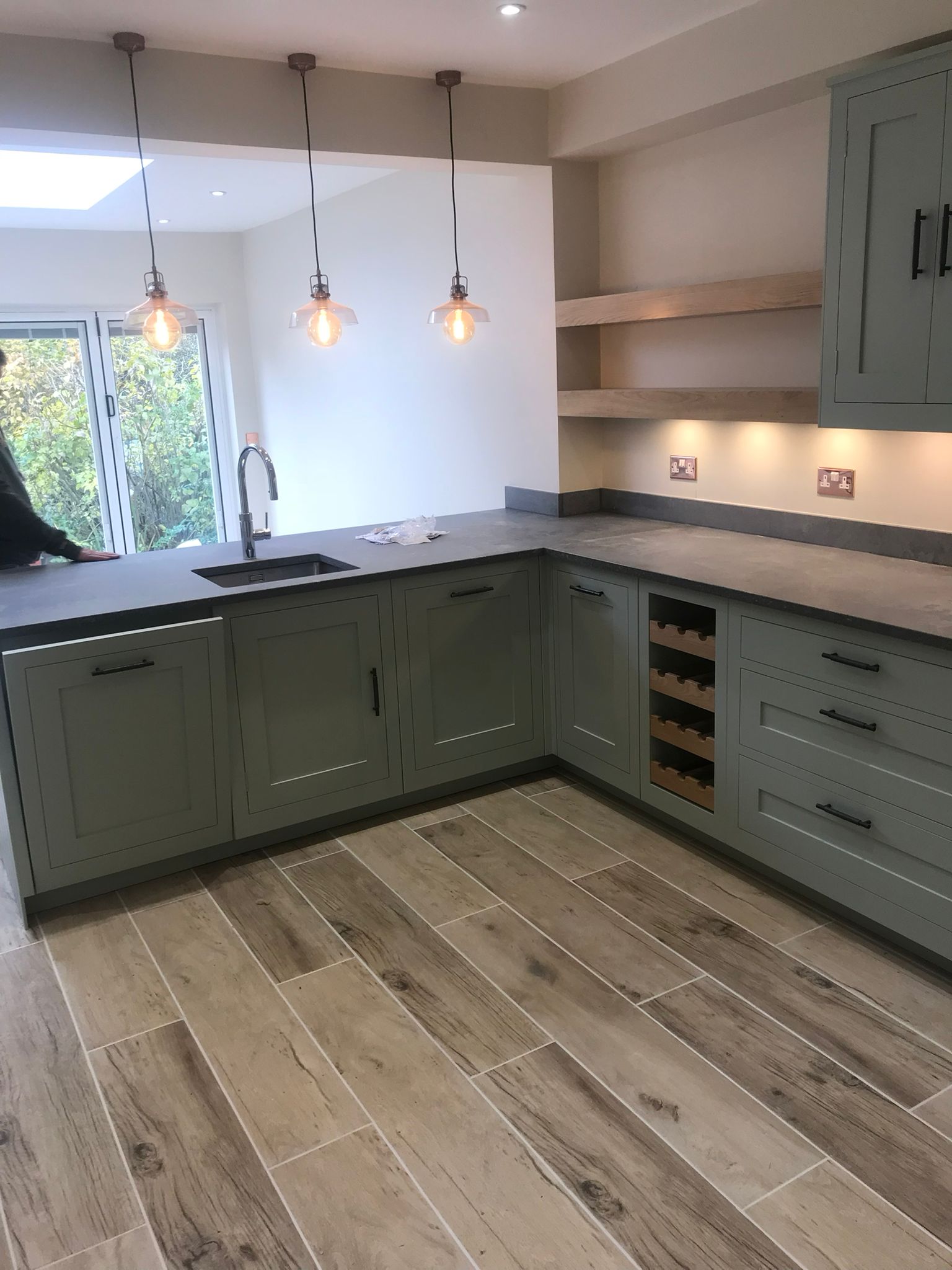 Completed kitchen with green fitted units and tiled backsplash